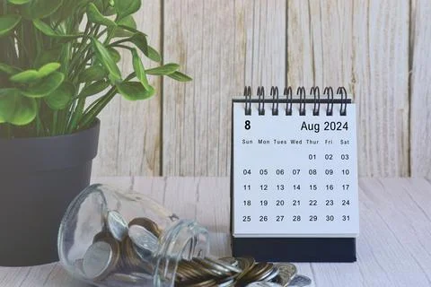 August 2024 desk calendar with stack of coins and potted plant on wooden desk. Stock Photos