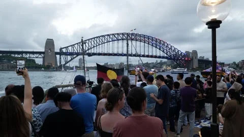 Australia Day crowds watch Aboriginal flag on boat in Sydney Harbour pass by Stock Footage 330583057