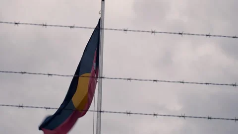 Australian Aboriginal flag framed by barbed wire on a windy, overcast day. Stock Footage 272610041