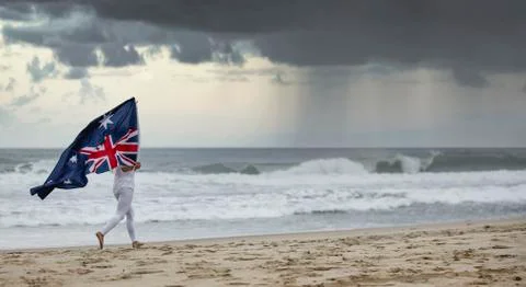 Australian flag blowing in wind held by a female jogging on a Aussie beach Stock Photos