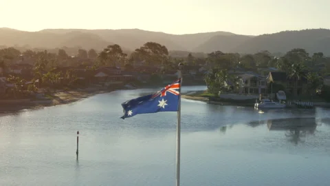 Australian flag blowing in the wind over scenic water views at sunrise Stock Footage 149718839