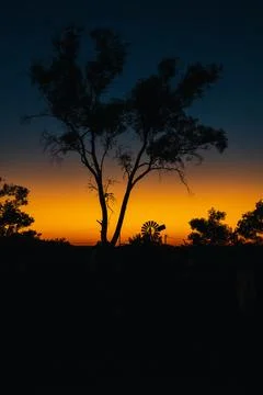 Australian outback sunset with old windmill silhouette casting an orange glow Stock Photos