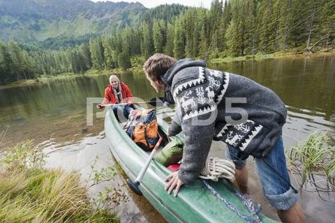 Austria, Obertauern, Young couple pushing kayak into lake Stock Photos