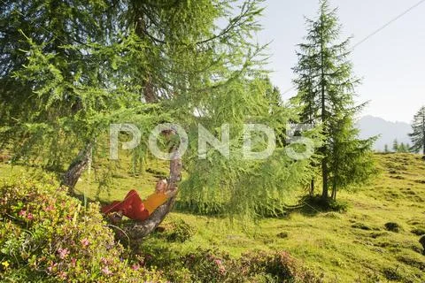 Austria, Salzburg County, Young woman leaning on tree in alpine meadow Stock Photos