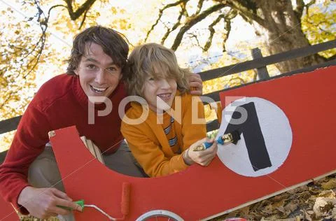Austria, Salzburger Land, Man and boy (12-13) painting soapbox, smiling Stock Photos