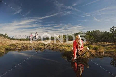 Austria, Salzburger Land, Woman relaxing by lake, bikers in background Stock Photos