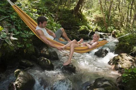 Austria, Steiermark, Young couple lying in hammock above stream Stock Photos
