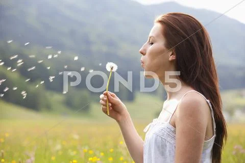 Austria, Young Woman Blowing Dandelion In Field Of Flowers