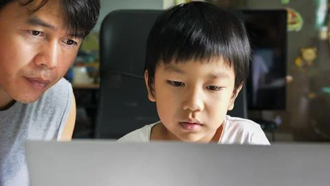 Authentic asian child boy using laptop with father with serious face. Stock Photos