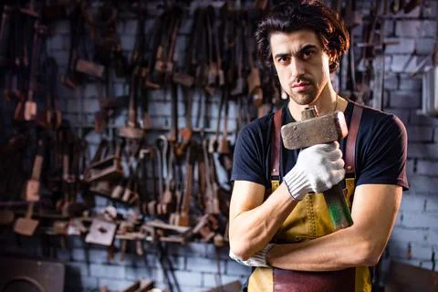Authentic blacksmith man forges a metal product in dark indoors studio Stock Photos