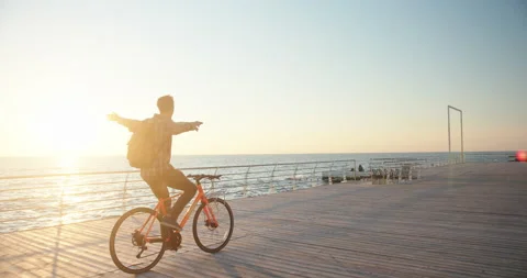 Authentic creative shot of a man cycling bicycle with hands up in air at sea Video stock 163887013