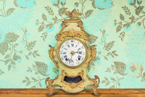 Authentic eighteenth century weathered table clock in front of wallpaper with Stock Photos
