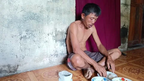 Authentic footage of a poor man eating a meal on the floor of his simple house. Stock Footage 317934793