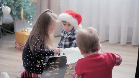 Authentic happy Joy children open box with gifts rejoice by Christmas tree play Stock Footage 152983076