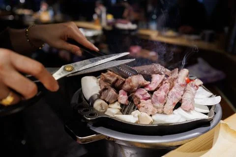 Authentic Korean BBQ Experience, Hands Cutting Meat on Grill Stock Photos