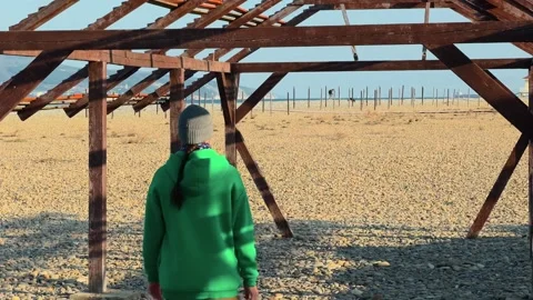 Authentic Man Walking Away Inside Abandoned Wooden Frame On Pebble Beach Te.. 스톡 동영상 330857378