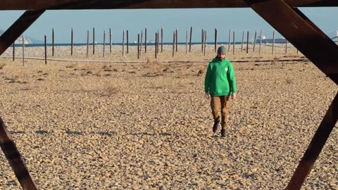Authentic Man Walking Toward Camera Through Wooden Arch On Pebble Beach Wit.. 스톡 동영상 330857471