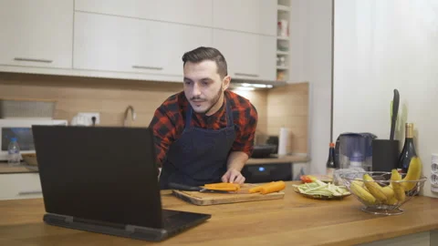  authentic moment of man in apron reading recipe from a laptop Stock Footage 143789564