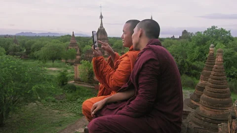 Authentic real monks, using smart phone to view video or photo of sunrise. Over Stockbeeldmateriaal 201094807