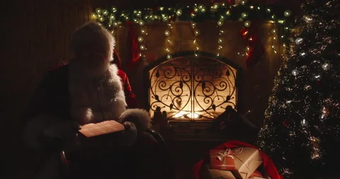 Authentic santa claus sitting in his rocker near fireplace, opening up a magical Stock-Footage 133354045