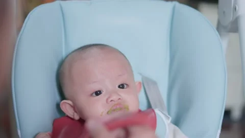 Authentic shot of cute asian newborn baby eating meal sitting on high chair.  Video stock 218291024