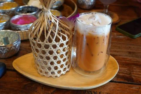 Authentic Thai iced milk tea with foam and a traditional bamboo woven cover  库存照片