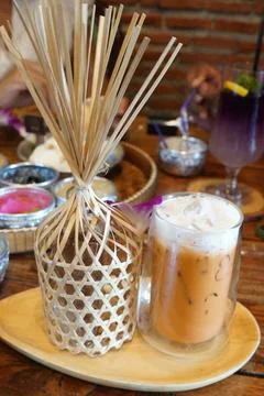 Authentic Thai iced milk tea with foam and a traditional bamboo woven cover  库存照片