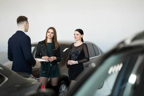 Auto business, car sales - a couple of friends of girls with a car dealer choose Stock Photos