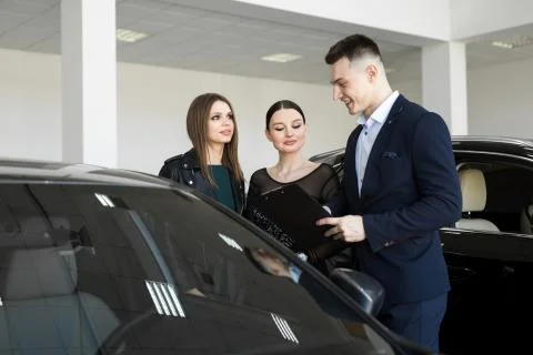 Auto business, car sales - a couple of friends of girls with a car dealer choose Stock Photos