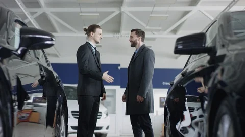 Auto dealership customer is shaking hands with male auto dealer. A male bearded Stock Footage 128589936