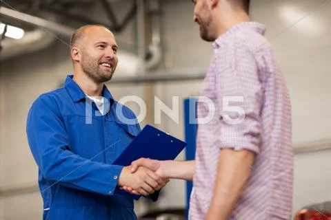 Auto mechanic and man shaking hands at car shop Stock Photos