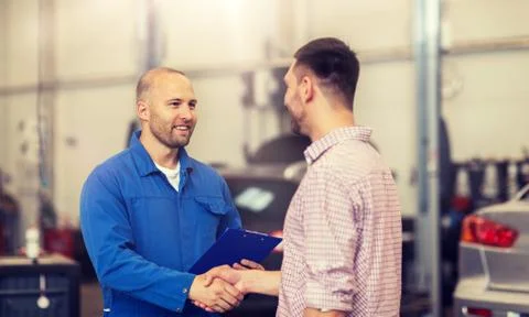 Auto mechanic and man shaking hands at car shop Stock Photos