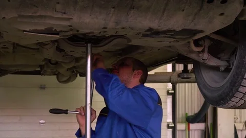 Auto mechanic in blue overals repairs car on the lift in garage Stock Footage 75687017