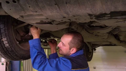 Auto mechanic in blue robe repairs car suspension in garge close-up Stock Footage 75687088