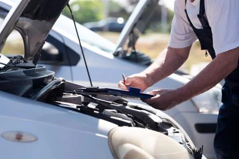 Auto mechanic checking car engine and writing on the clipboard Stock Photos