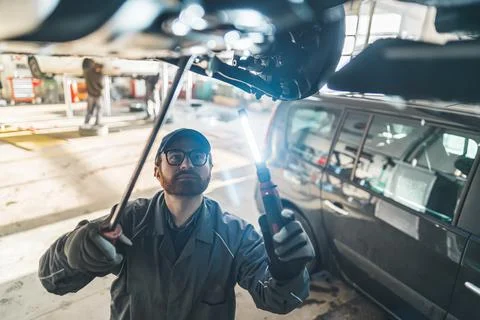 Auto mechanic checking under car condition in garage Stock Photos
