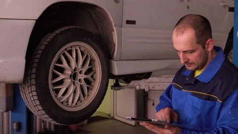 Auto mechanic conducts diagnostics of undercarriage with the help of a tablet Stock Footage 75687761