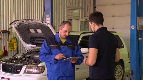 Auto mechanic diagnoses the car using a tablet in garage Stock Footage 75684113