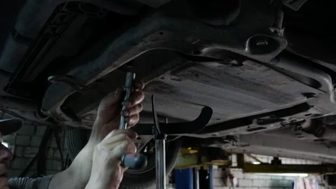 Auto mechanic with dirty hands working underneath car lifting machine at the gar Stock Footage 282958985