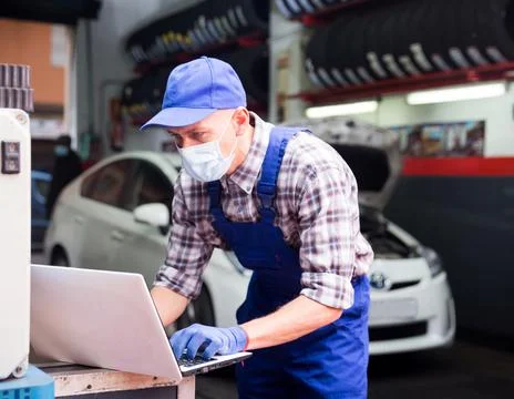 Auto mechanic in face mask using a laptop computer checking car Stock Photos