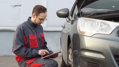 Auto mechanic holding digital tablet checking car wheel in auto service garage. Stock Footage 180679348