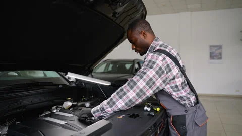 Auto mechanic inspecting car engine with work lamp Stock Footage 300610438