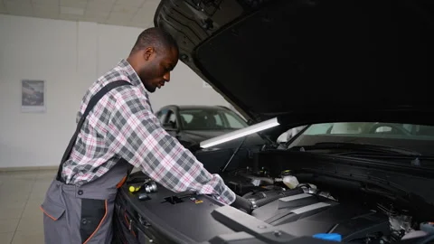 Auto mechanic inspecting car engine with LED work lamp Stock Footage 300610557