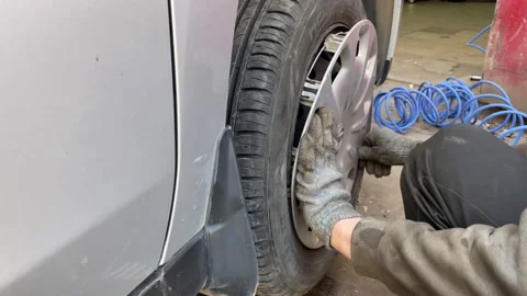Auto mechanic installs the cap on the wheel of the car Stock Footage 184874366