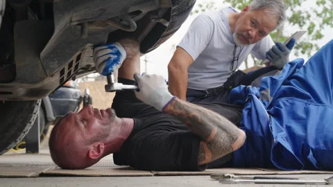 An auto mechanic laying down on the ground while his supervisor watching Stock Footage 246116805