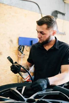 Auto mechanic pumps up a wheel with a compressor. Wheel repair. Tire service. Stock Photos