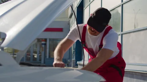 Auto mechanic in red overalls performing under-the-hood check on a car, Video stock 312516416