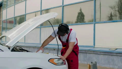 Auto mechanic in red overalls performing an under-the-hood check on a white car, Video stock 312517589