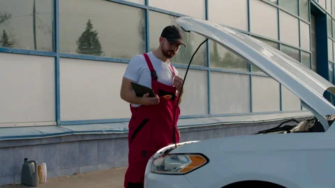 Auto mechanic in red overalls performs under-the-hood check on a vehicle, Video stock 312517028