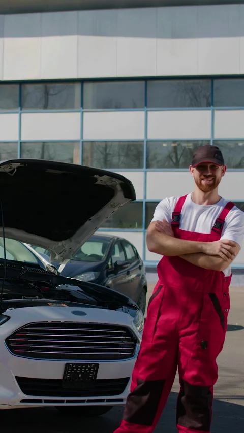 Auto mechanic in red overalls performs under-the-hood check on a white car Stock Footage 318346191